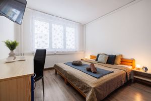 Manželská postel s hnědou přikrývkou a dlouhý psací stůl u okna