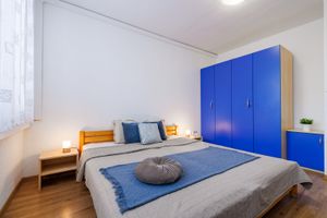Manželská postel se šedou přikrývkou před modrou skříní