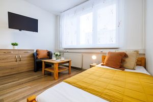 Jednolůžkový pokoj s hořčicovým přehozem, televizí a komodou
