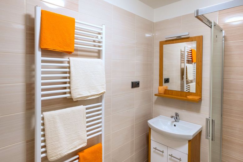 Koupelna s béžovým obkladem, sprchovým koutem a oranžovými ručníky na žebříku