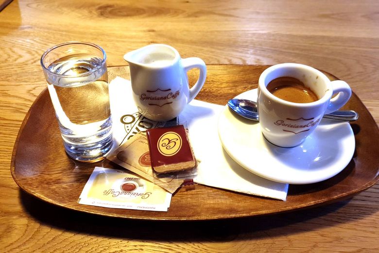 Espresso, konvička mléka a sklenice vody na dřevěném tácu