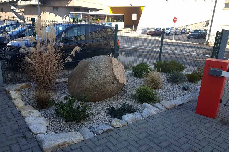 Okolí vstupu do hotelu: kamenný záhon se štěrkem, za plotem zaparkovaná auta a autobusový terminál